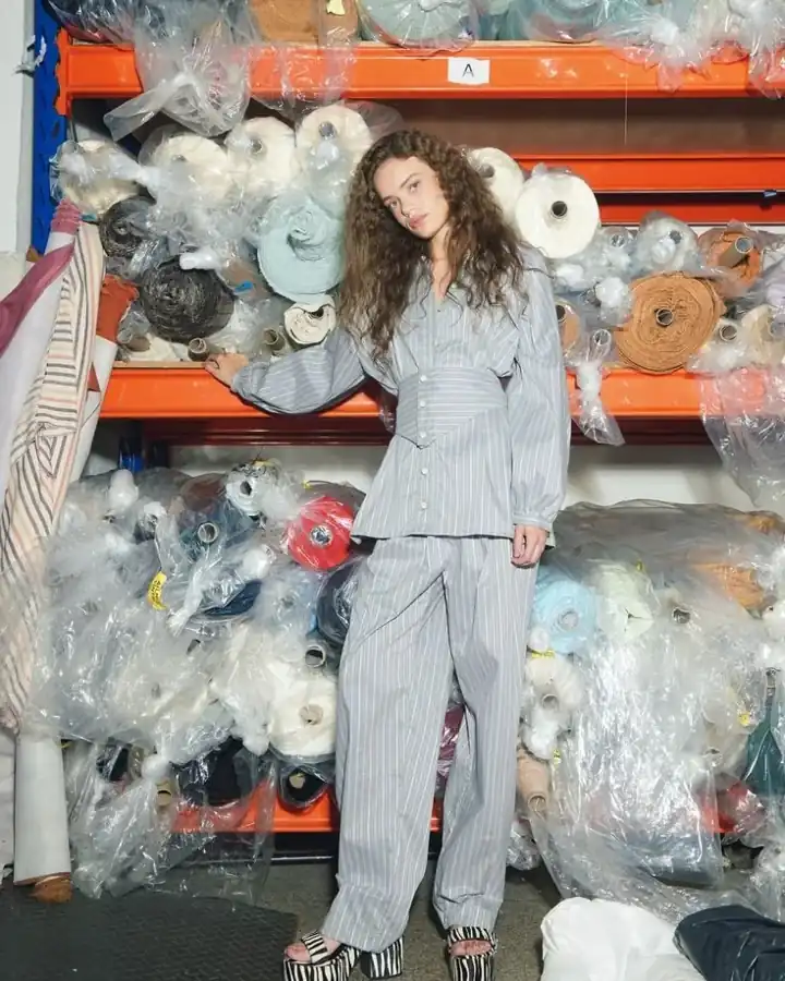 Model in a grey set in front of racks of fabric rolls, fabric and trim sourcing for garment manufacturing, DRESSOURCE